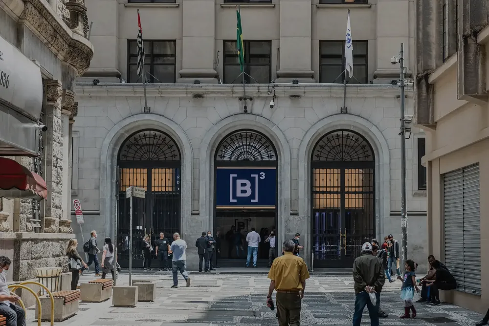 Fachada da B3 em São Paulo, com pessoas na calçada.